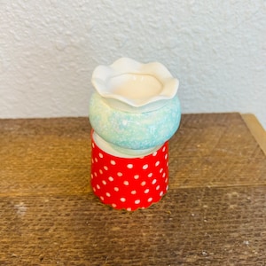 May include: A white ceramic diffuser with a scalloped top and a blue and white speckled base. The diffuser is sitting on a red polka dot base.