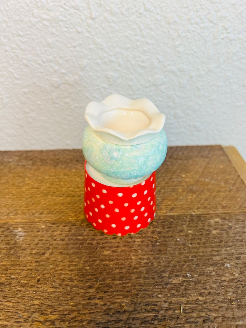 May include: A white ceramic diffuser with a scalloped top and a blue and white speckled base. The diffuser is sitting on a red polka dot base.