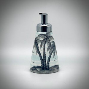 May include: A ceramic soap dispenser with a silver pump top. The dispenser is decorated with a blue and white striped background and a black and white illustration of palm trees.
