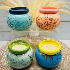 May include: Four colorful ceramic planters with speckled glaze and contrasting colored rims. The planters are in shades of blue, green, yellow, and orange.