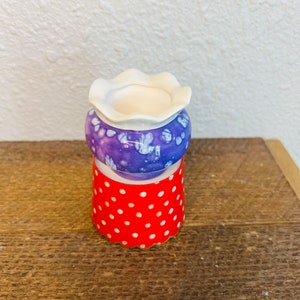 May include: A small purple and white ceramic planter with a white rim sits on a red and white polka dot base.