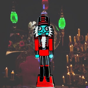 May include: A blue and red nutcracker figurine with a spooky, skeletal face. The figurine is standing on a red base and has a black and white striped pattern on its legs.