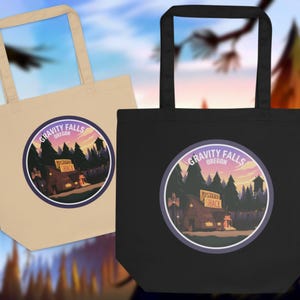 Peut inclure: Deux sacs fourre-tout, un beige et un noir, chacun avec un graphisme circulaire. Le graphisme affiche les mots "Gravity Falls Oregon" autour d'une cabane et d'arbres, avec le texte "Mystery Shack".