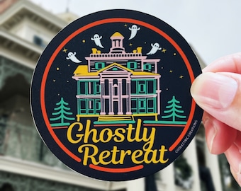 May include: Round sticker with a black background and an orange border. The sticker features a colorful illustration of a mansion with ghosts, trees, and the words "Ghostly Retreat" in yellow. The sticker is held by a hand.