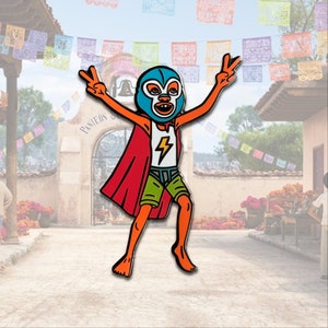 May include: A colorful enamel pin featuring a cartoon character in a luchador mask, red cape, and green shorts. The character is giving a peace sign with both hands. A white shirt with a lightning bolt is visible. The background shows a festive street scene.