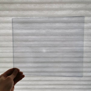 May include: A clear plastic sheet, held in a hand, against a white background.