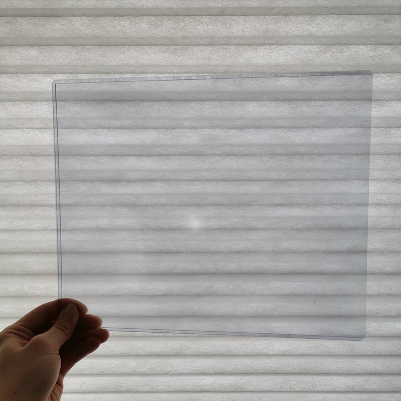 May include: A clear plastic sheet, held in a hand, against a white background.