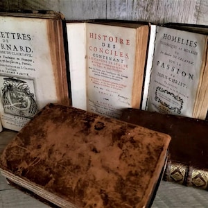 May include: A collection of antique books with aged, worn covers. Titles include "LES LETTRES", "HISTOIRE DES CONCILES", and "HOMELIES". The books are in various states of wear, with visible text and decorative elements.