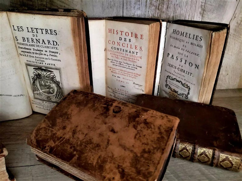 May include: A collection of antique books with aged, worn covers. Titles include "LES LETTRES", "HISTOIRE DES CONCILES", and "HOMELIES". The books are in various states of wear, with visible text and decorative elements.