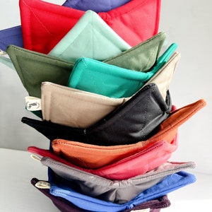 May include: A stack of 10 quilted pot holders in various colors, including red, green, blue, brown, and black. The pot holders are folded in a triangular shape and stacked on top of each other.