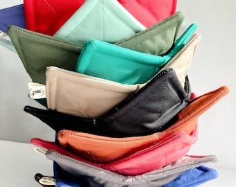 May include: A stack of 10 quilted pot holders in various colors, including red, green, blue, brown, and black. The pot holders are folded in a triangular shape and stacked on top of each other.
