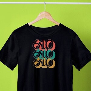 May include: Black t-shirt with a stacked design of the number "610" in different colors, including teal, orange, and pink.
