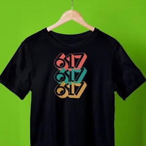 May include: Black t-shirt with a graphic design of the number 617 repeated three times in different colors: pink, teal, and orange.
