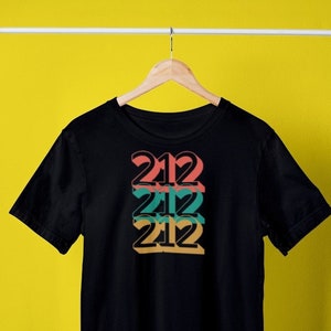 May include: Black t-shirt featuring a graphic design of the number 212 repeated three times in a stacked, offset pattern. The numbers are in shades of red, orange, yellow, and green.