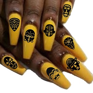 May include: Close-up of a hand with long, yellow nails decorated with black African tribal mask nail art decals.