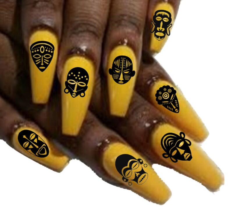 May include: Close-up of a hand with long, yellow nails decorated with black African tribal mask nail art decals.