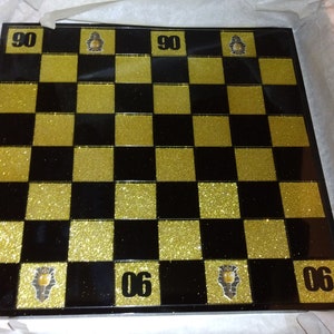 May include: A black and gold checkerboard with glitter. The numbers 90 and 06 are printed on the board.