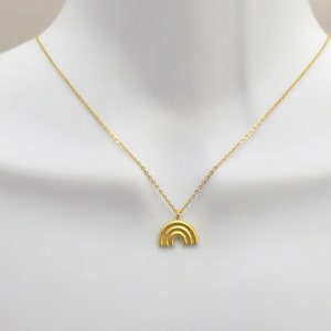 May include: A gold chain necklace with a small, gold, rainbow-shaped pendant.