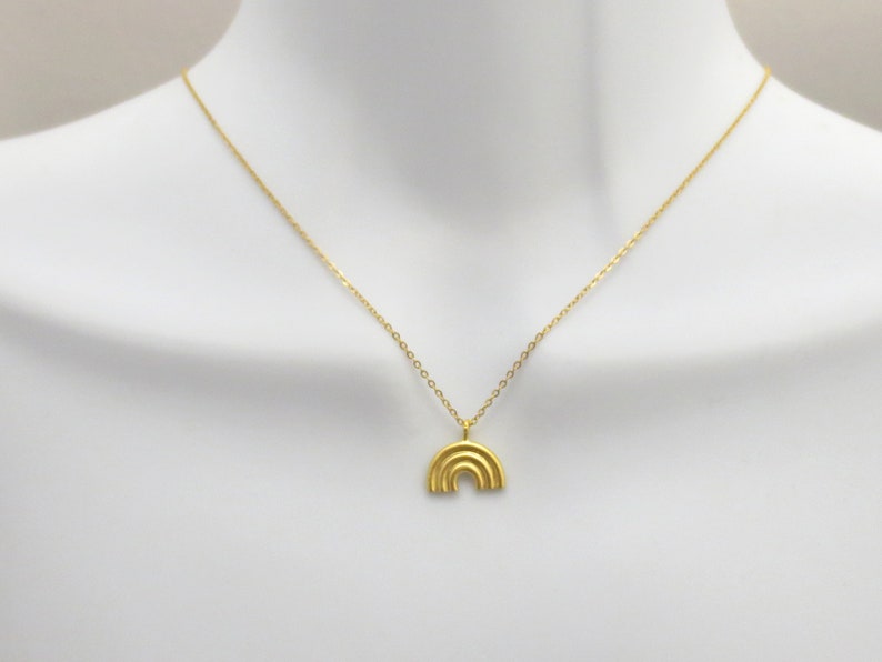May include: A gold chain necklace with a small, gold, rainbow-shaped pendant.