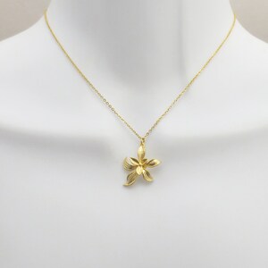 May include: A gold chain necklace with a delicate flower pendant. The flower is made of gold and has a detailed design.