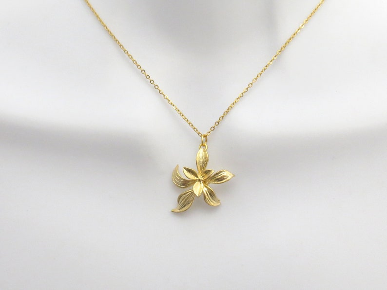 May include: A gold chain necklace with a delicate flower pendant. The flower has five petals and is made of a textured metal.