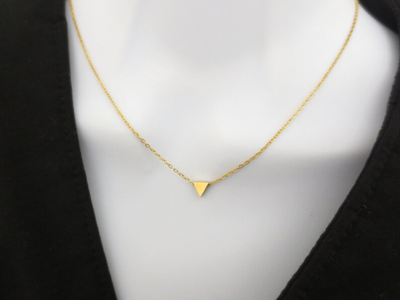 Puede incluir: Un collar de cadena dorada con un peque&ntilde;o colgante triangular.
