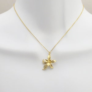 May include: A gold chain necklace with a delicate flower pendant. The flower is made of gold and has a textured surface.