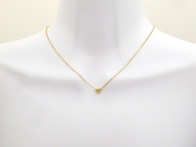 Puede incluir: Un collar de cadena dorada con un peque&ntilde;o colgante triangular.