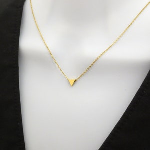 Puede incluir: Un collar de cadena dorada con un peque&ntilde;o colgante triangular dorado.