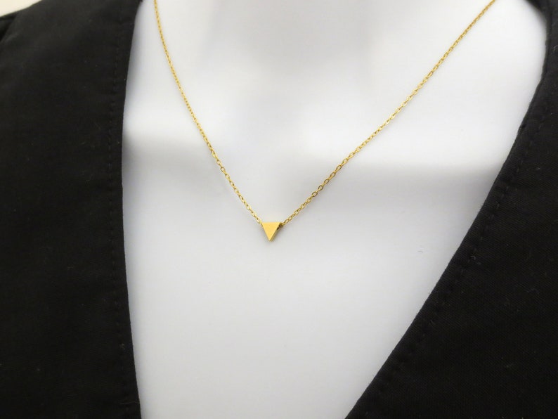 Puede incluir: Un collar de cadena dorada con un peque&ntilde;o colgante triangular dorado.