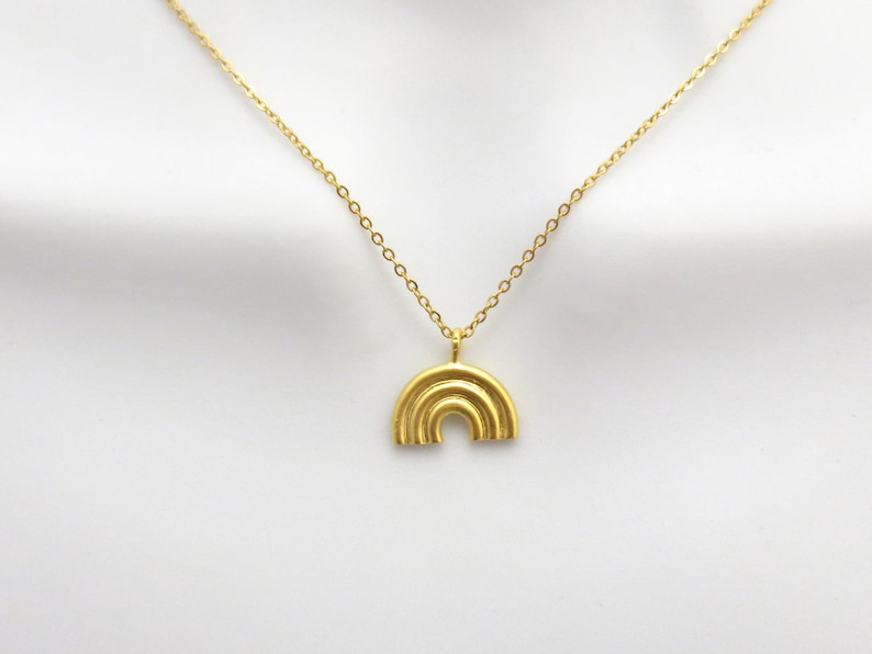 May include: A gold chain necklace with a rainbow pendant. The pendant is made of multiple layers of gold metal.