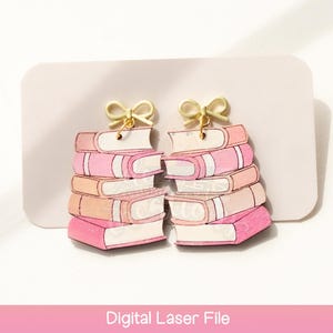 Puede incluir: Pendientes con forma de pilas de libros. Cada pendiente presenta cinco libros en tonos rosa y blanco, coronados por un lazo dorado. Los pendientes están sobre un fondo blanco. El texto "Digital Laser File" está en la parte inferior.