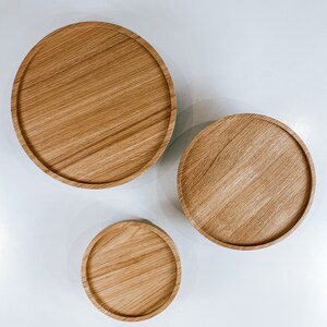 May include: Three round wooden trays of varying sizes, arranged in a descending order from left to right. The trays are made of light brown wood with a natural grain pattern.