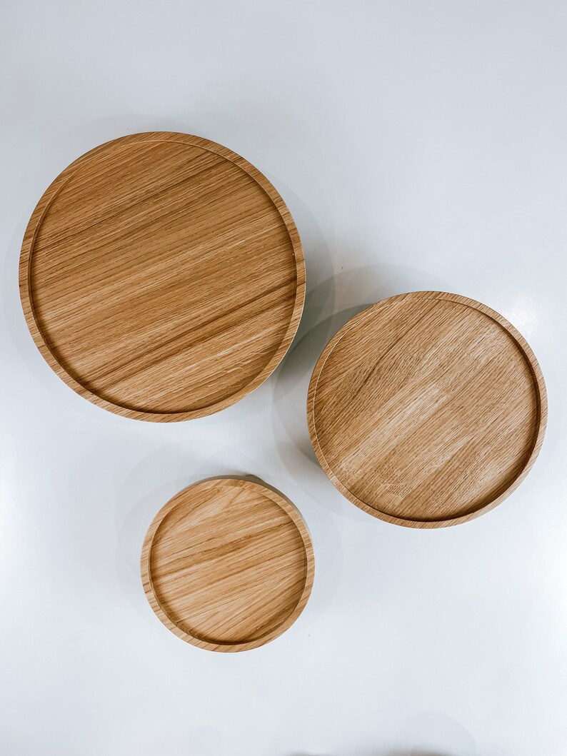 May include: Three round wooden trays of varying sizes, arranged in a descending order from left to right. The trays are made of light brown wood with a natural grain pattern.