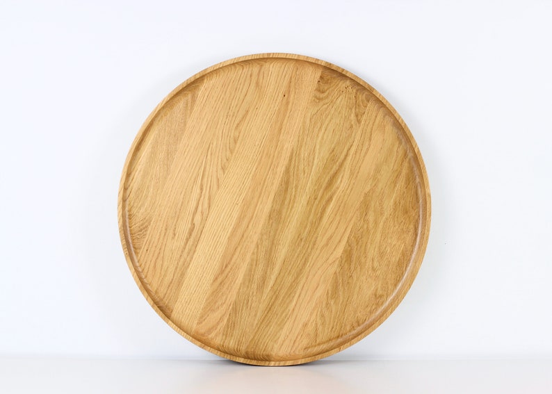 Handcrafted round oak serving tray with raised edge, displayed on a white surface.