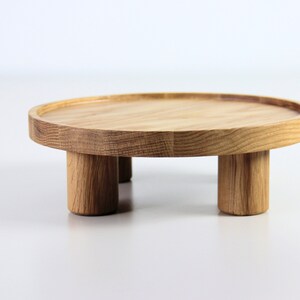 May include: A round wooden tray with three legs. The tray is made of light brown wood and has a natural finish.