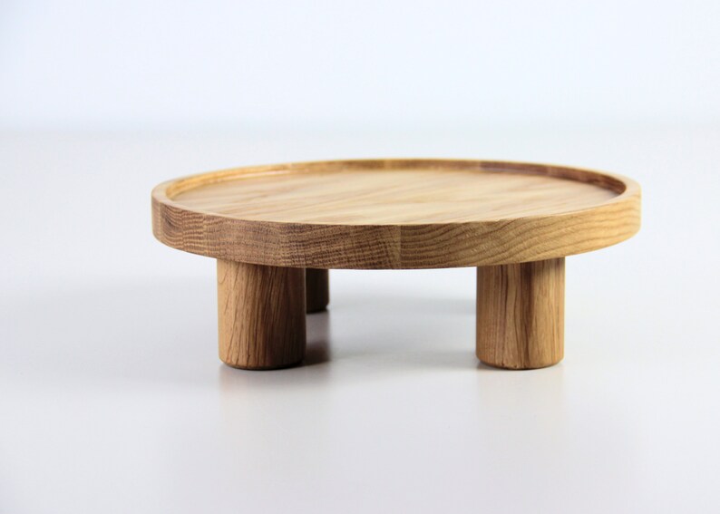 May include: A round wooden tray with three legs. The tray is made of light brown wood and has a natural finish.
