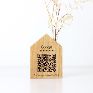 Peut inclure: Un vase en bois en forme de maison avec un code QR et le logo Google. Le vase est en bois clair et contient des fleurs séchées. Le texte "Share your experience" est en dessous du code QR.