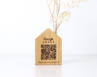 May include: A wooden house-shaped vase with a QR code and the Google logo. The vase is made of light-colored wood and has dried flowers. The text "Share your experience" is below the QR code.