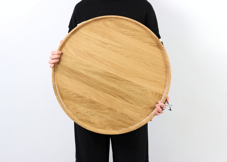 Person holding a large round oak wood serving tray in front of their body, showcasing the natural grain and smooth finish of the wood.