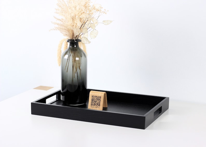 Modern minimalist black serving tray with QR code menu stand and smoky glass vase. The rectangular tray features clean lines and cut out handles. Perfect for restaurant, café, or home décor. Shot against a white background.