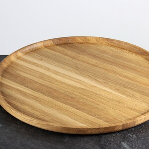 Side view of a round oak wood serving tray placed on a table, showcasing its raised edge and natural wood texture.