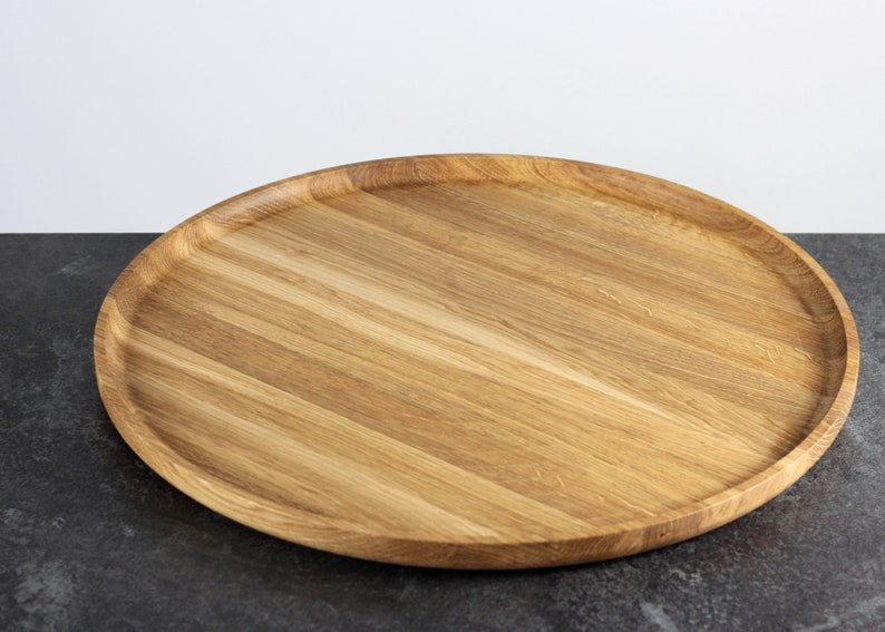 Side view of a round oak wood serving tray placed on a table, showcasing its raised edge and natural wood texture.