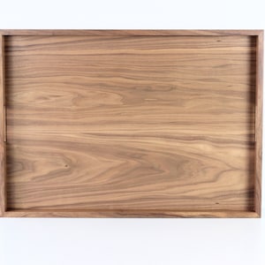 Puede incluir: Una bandeja rectangular de madera con un acabado de madera natural. La bandeja tiene un borde elevado y est&aacute; hecha de madera maciza.