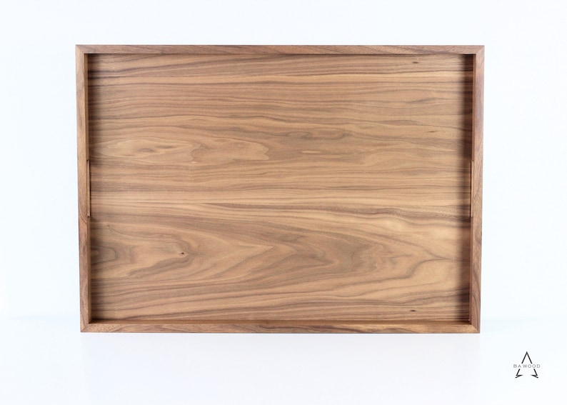 Puede incluir: Una bandeja rectangular de madera con un acabado de madera natural. La bandeja tiene un borde elevado y est&aacute; hecha de madera maciza.
