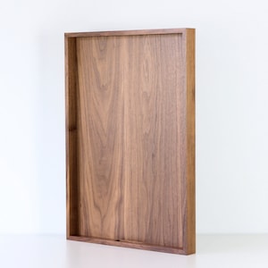 Puede incluir: Una bandeja rectangular de madera de nogal. La bandeja tiene un acabado de madera natural y es perfecta para servir comida o bebidas.