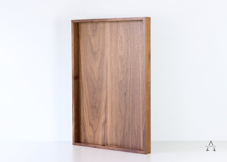 Puede incluir: Una bandeja rectangular de madera de nogal. La bandeja tiene un acabado de madera natural y es perfecta para servir comida o bebidas.