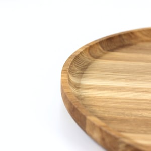 Close-up of a round oak wood serving tray showing natural wood grain patterns and smooth finish.