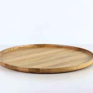 Side view of a round oak wood serving tray placed on a table, showcasing its raised edge and natural wood texture.