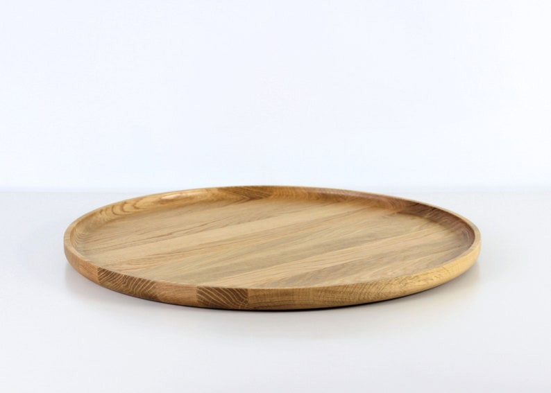 Side view of a round oak wood serving tray placed on a table, showcasing its raised edge and natural wood texture.